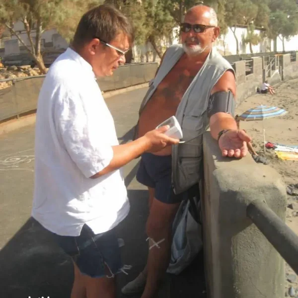 Kahe mehe vestlus rannas, üks näitab telefoni, teine naeratab, päikeseline päev.